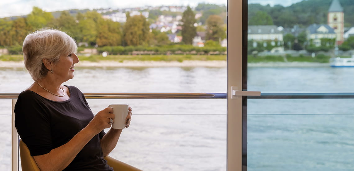 A woman enjoying a hot drink on the balcony of her cabin on Spirit of the Rhine